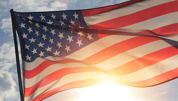 American flag blowing in the wind with sunlight behind it.