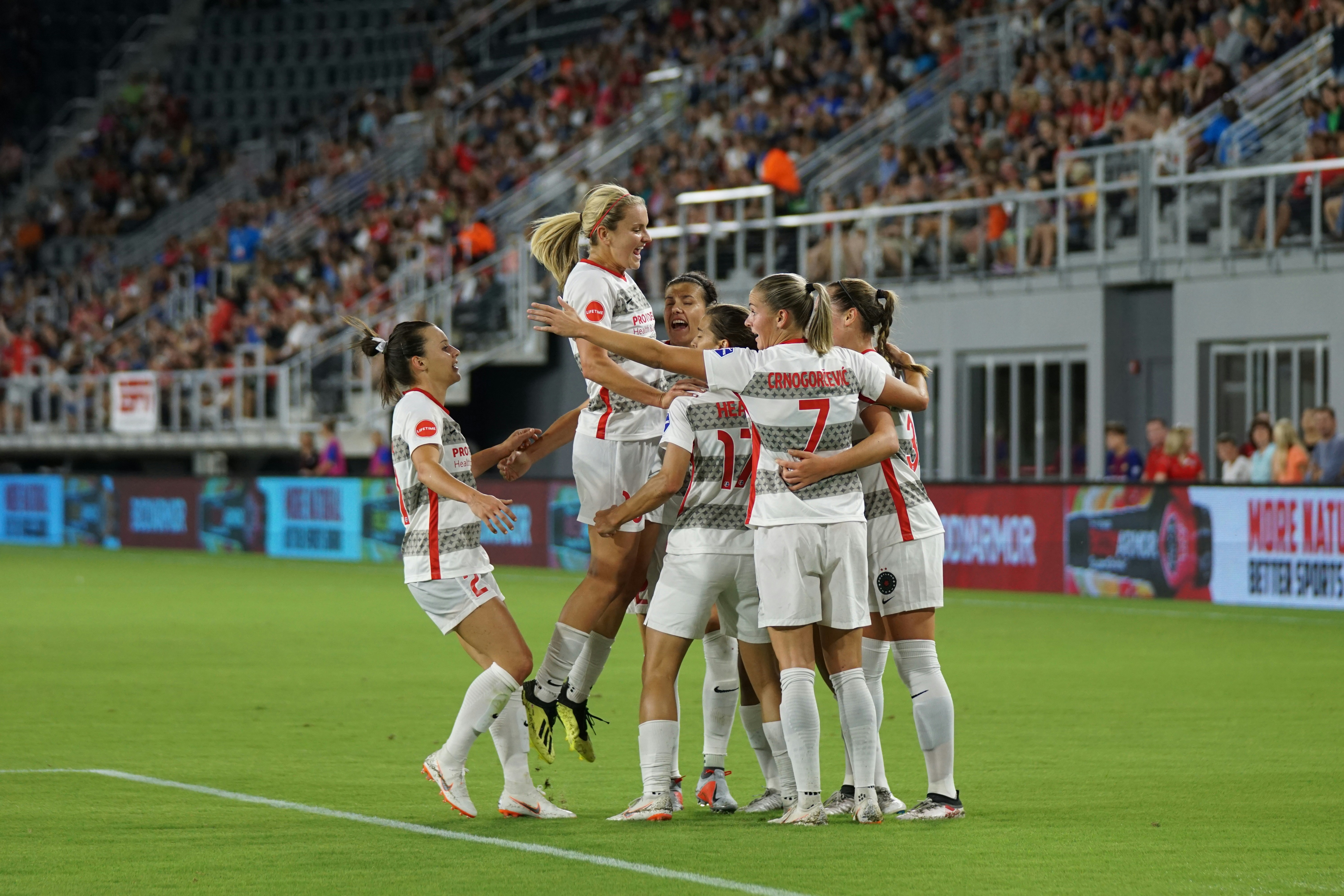 Women’s soccer team on soccer field, celebrating as a group.